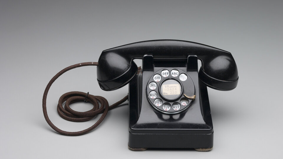 A black telephone with a rotary dial sits on a grey backdrop