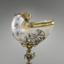 A stemmed cup. The cup itself resembles a shell. It has an iridescent surface that is decorated with images of insects as well as a scene involving four figures. The opening faces directly up and is fitted with a flared, gold-colored lip. A curved section of the shell rises vertically above and alongside the opening and terminates in a gold-colored face, perhaps that of a bird. The shell is supported underneath by an ornate stem on a broad, two-tiered base.