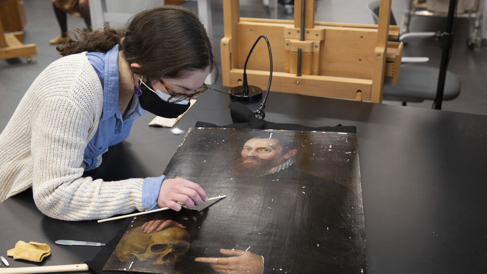 Amanda Kasman using a swap to clean the surface of the panel painting, which rests on a black table in the conservation lab.