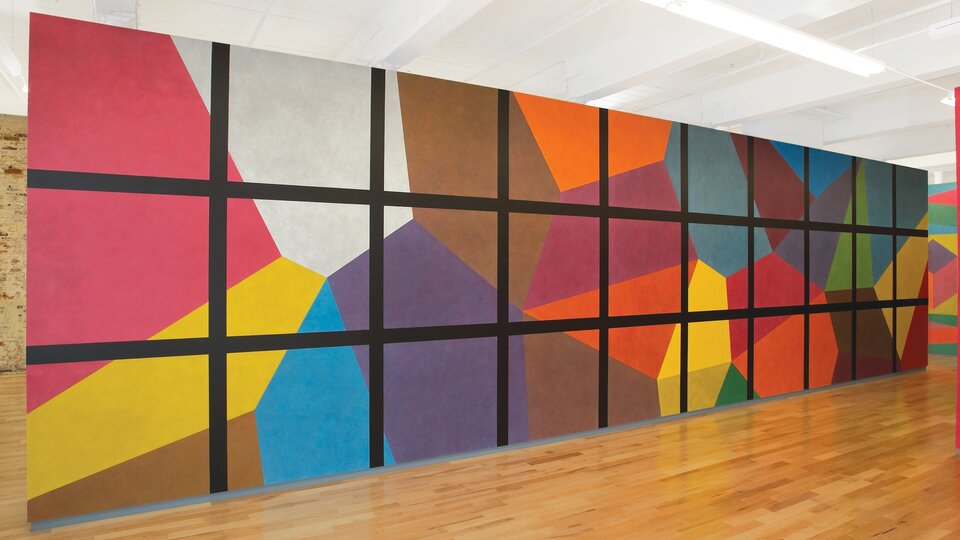 A wall drawing made up of bright, colorful isometric cubes overlaid with a square black grid