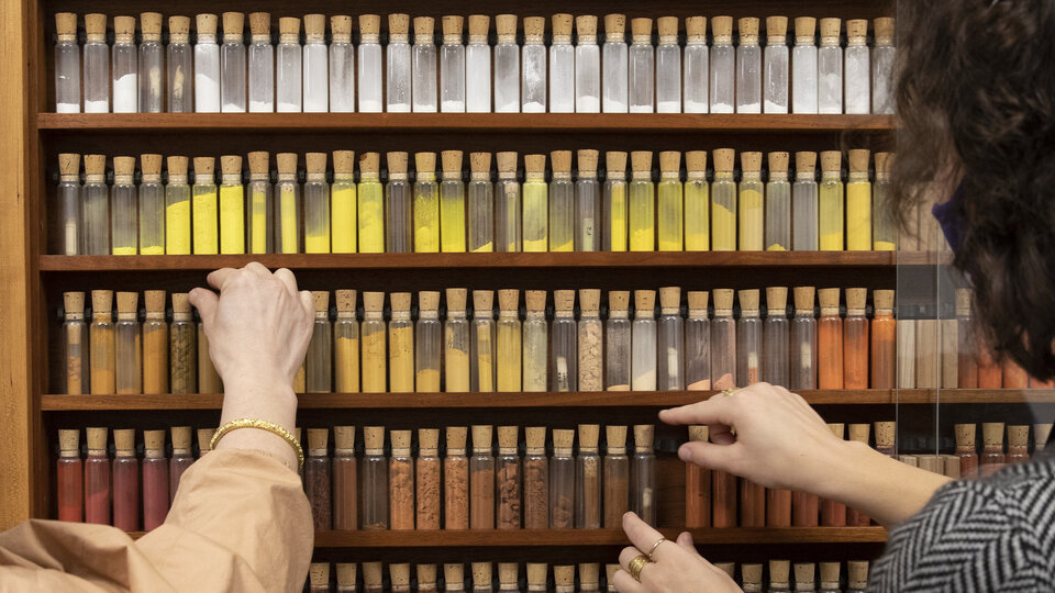 Two people looking at a row of glass vials filled with colored pigments