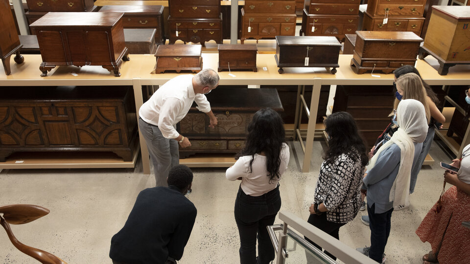 Male staff member leading visitors on a tour of the American furniture collection. 
