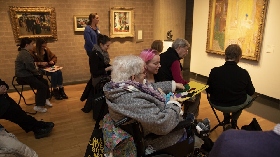 A woman in a wheelchair watches a person looking at art