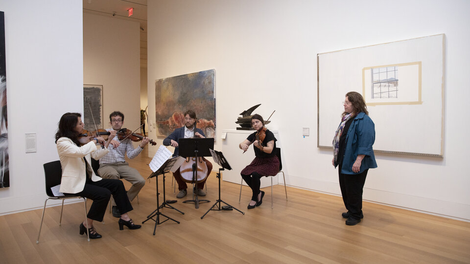 A string quartet plays in a white walled room filled with art