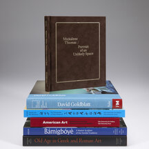 Five books stacked horizontally with the spine facing outward. A book with a dark brown cover with the title is framed by a rope-like pattern rests upright atop the stack. 