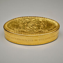 A gold oval box with elaborate engraving, including the seal of the City of New York on its lid.