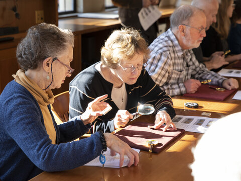 Visitors examining coins with magnifying glasses.