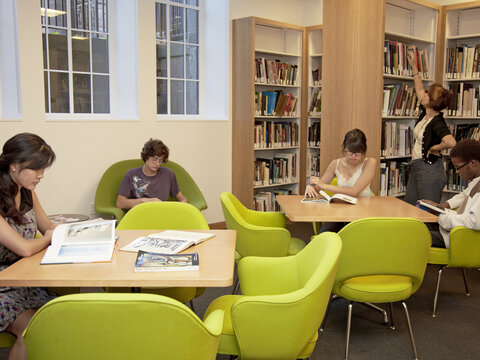 Young people sitting at tables and reading books in the Nolen Center Library..