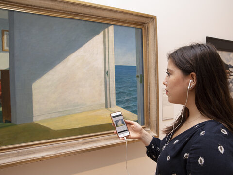 A Gallery visitor looking at a painting and listening to an audio guide.