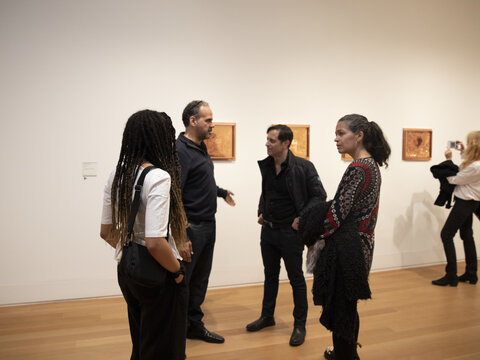 Four visitors in conversation at the Matthew Barney exhibition, with a women in the background taking a photo of one of the works on view.
