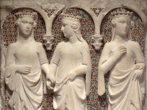 A row of three standing, marble female figures with crowns set in front of mosaic background and framed by arches.