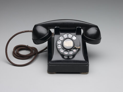A black telephone with a rotary dial sits on a grey backdrop