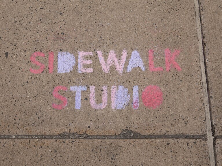 a photo of the ground, written in colorful chalk, "Sidewalk Studio".