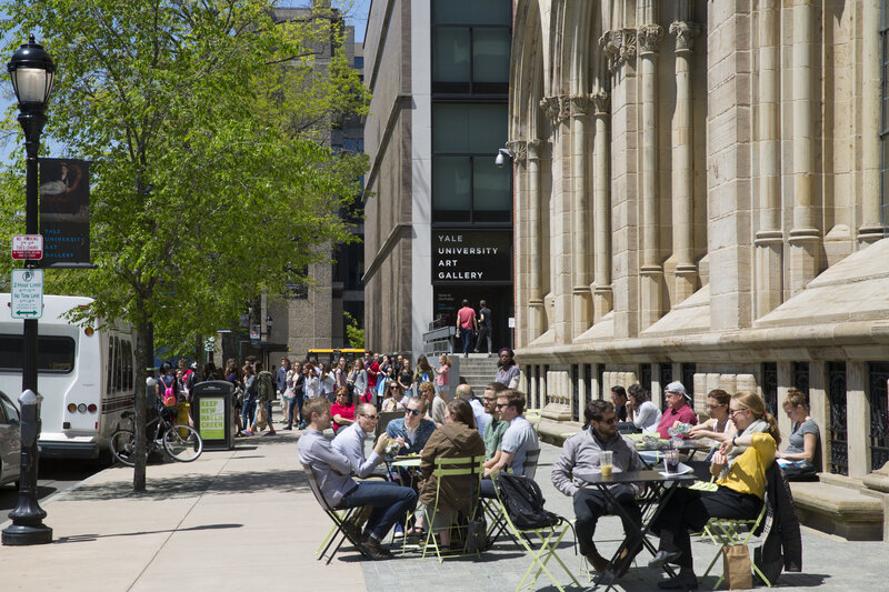 Crowds of people sit outdoors at bistro tables on a sidewalk alongside the museum