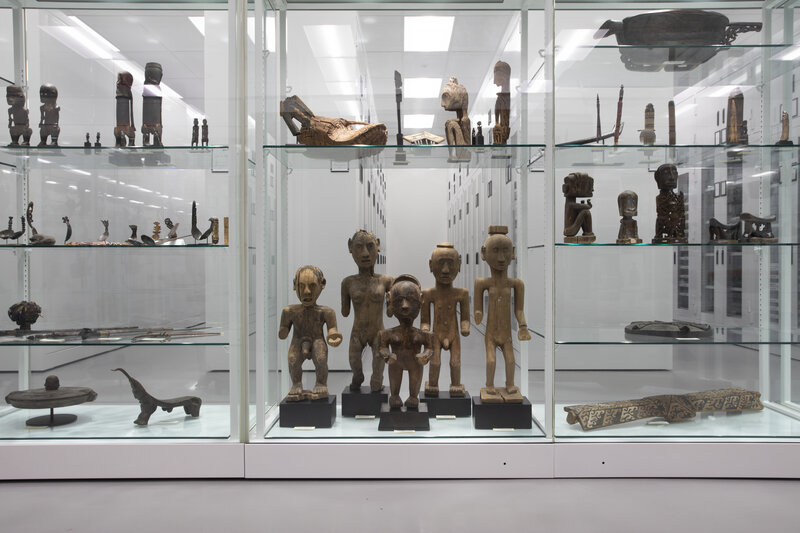 Wooden objects, many figurative, in glass cases on shelves