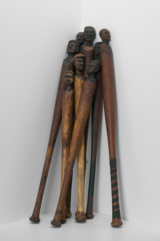 Baseball bats, sculpted with faces, leaning in a corner.