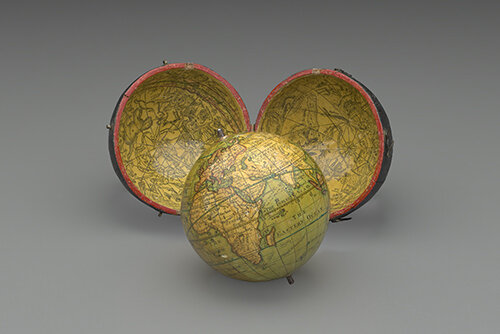 A globe resting on a surface in front of its case. The case consists of two semicircles, possibly hinged. The yellowish-green interior of the case is covered with lines and ornamentation.