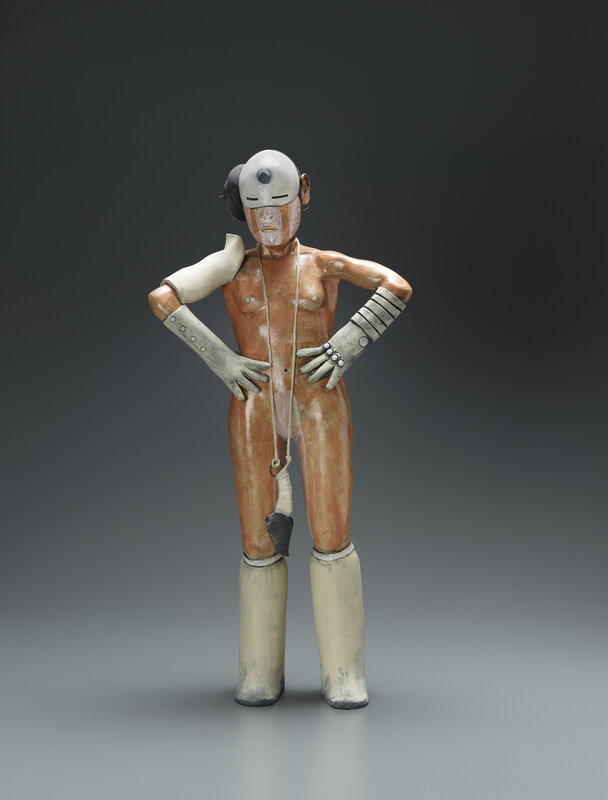 A sculpture shaped like a human figure with arms akimbo. The figure wears knee-high boots and elbow-length gloves, as well as a cuff on their right shoulder and a mask over the upper part of their face. 